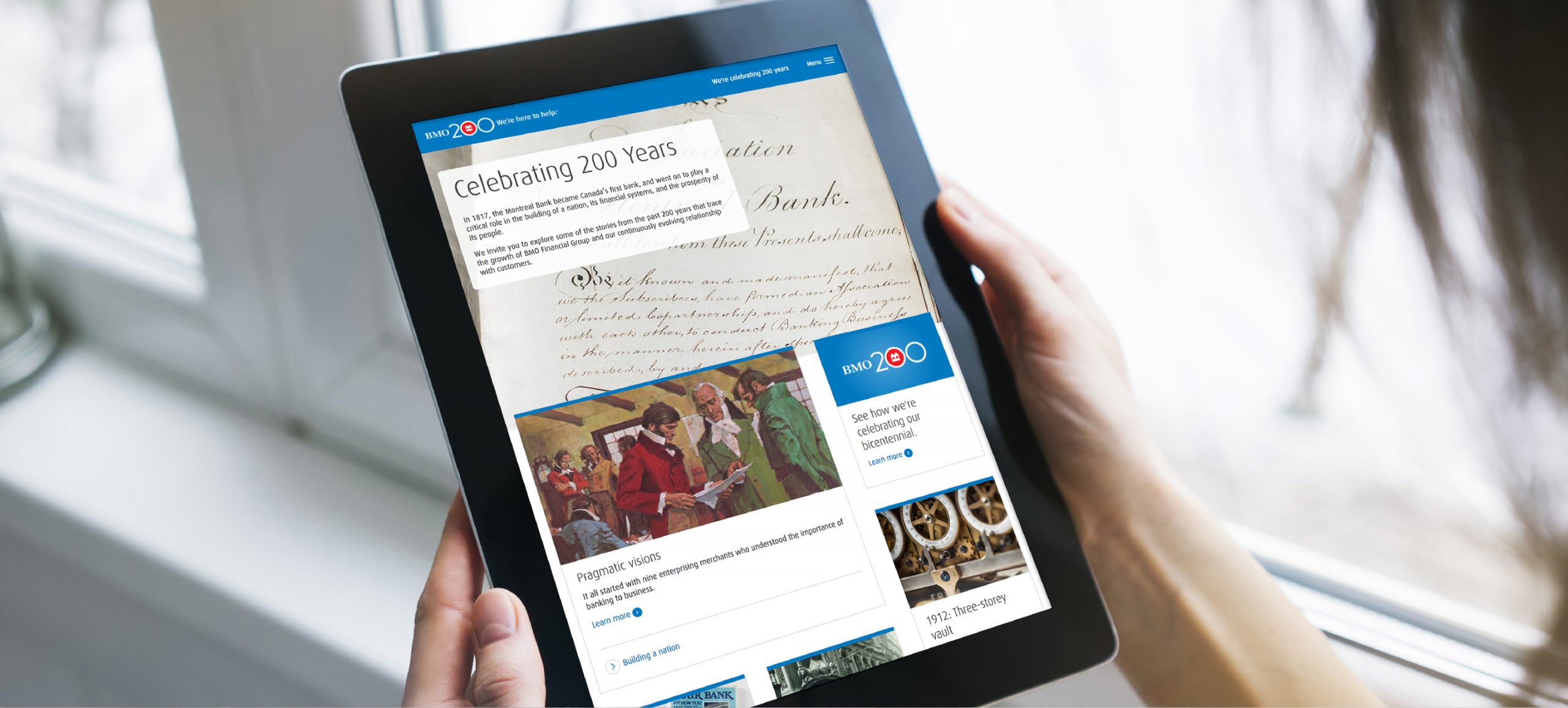The BMO history website is shown being viewed by a woman using a tablet device.