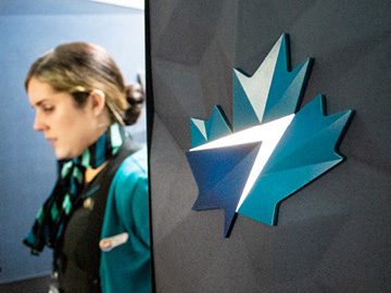 Image of the cabin interior of a WestJet's airplane. A lit-up WestJet maple leaf logo can be seen on the wall, and a flight attendant is passing by in the background.