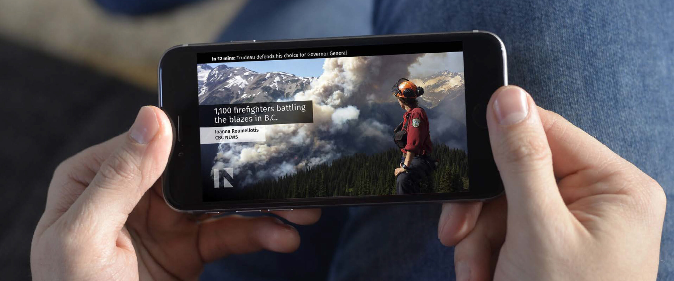 Closeup of a person holding a mobile phone that shows a live stream of The National and its onscreen graphics