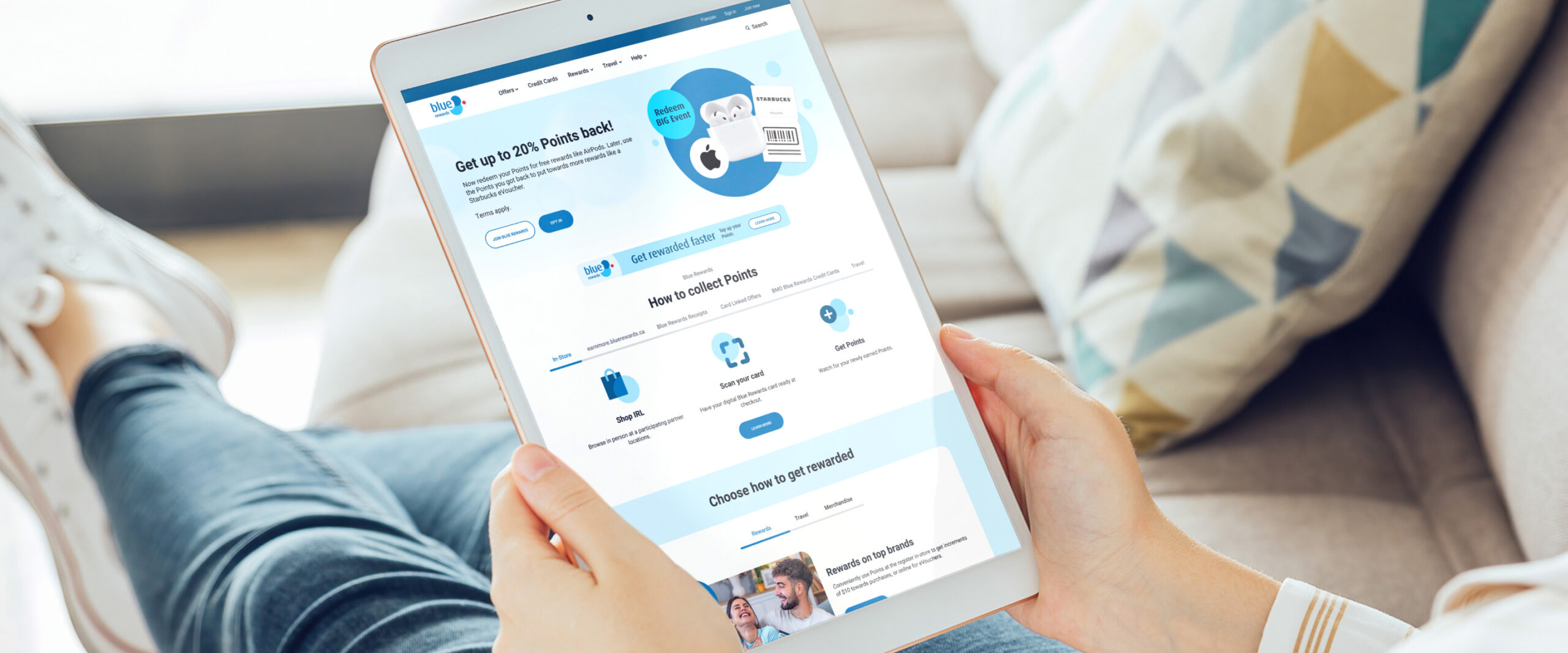 Closeup of a person sitting on a couch, holding a table where the Blue Rewards website can be seen on the screen